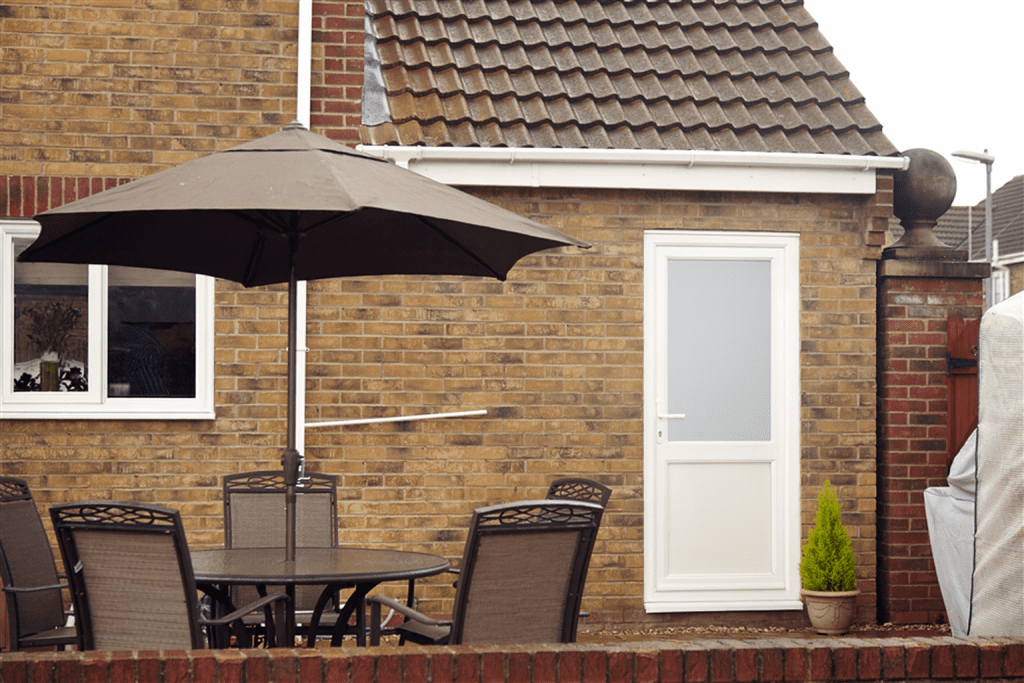Backyard with white uPVC door featuring frosted glass and brown patio furniture under a large umbrella.