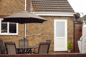 Backyard with white uPVC door featuring frosted glass and brown patio furniture under a large umbrella.